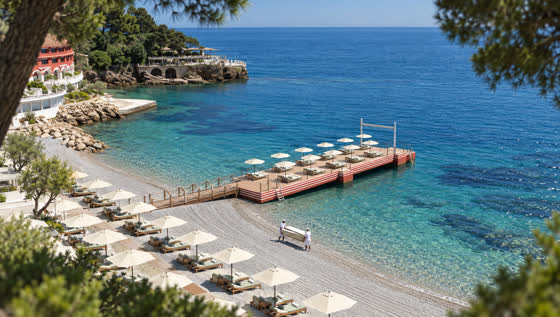 The private beach from above, umbrella rows raked and ready, two attendants carrying a daybed